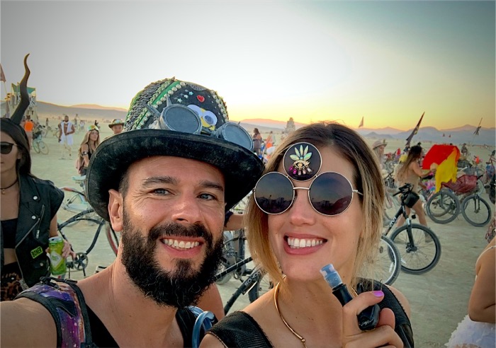 Two figures in hand-decorated hats and goggles, out in the desert at sunset